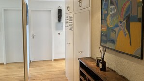 A hallway with wooden flooring, a wooden cabinet with a bottle and reed diffuser, a painting on the wall, and a security camera.
