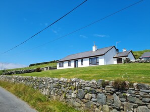 A white house with a grey roof, a stone wall, and a clear blue sky. - Sea View Cottage, Errislannan (Clifden)
