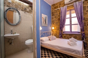Classic design with a checkered floor, white bed, and stone wall, featuring a large mirror and sink.
