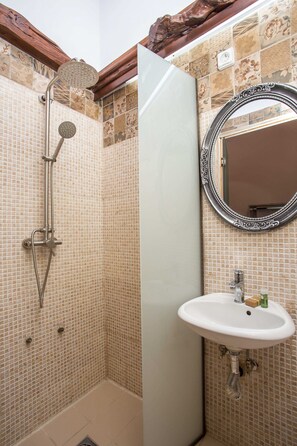 Bathroom features a shower area with handheld showerhead and wall-mounted faucet, a pedestal sink, and a rectangular mirror.