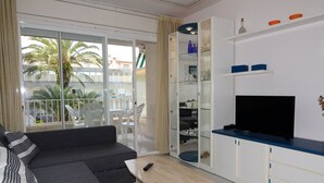 A modern living room with a sofa, a coffee table, a TV, and a glass door leading to a balcony with chairs. - ILLA MAR D'OR 148 (Estartit)