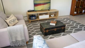 A living room with a sofa, a coffee table, a television on a wooden stand, and a bookshelf.