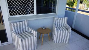 A small balcony with two striped armchairs and a round wooden table.