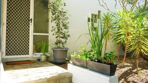 A house with a sliding glass door, a small porch with steps, and various potted plants.