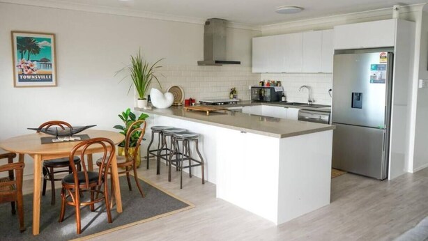 Une cuisine moderne dotée d’un îlot central, de meubles blancs, d’appareils électroménagers en acier inoxydable et d’un coin repas avec des chaises et une table en bois.
