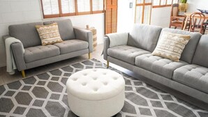 Un salon avec deux canapés gris, un pouf blanc et un tapis à motifs.