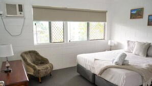 Une chambre à coucher comprenant un lit, une chaise, un bureau et une fenêtre avec des stores.