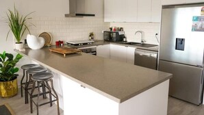 Une cuisine moderne avec des armoires blanches, un réfrigérateur en acier inoxydable, un four encastré et un îlot central doté de tabourets.