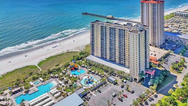 A high-rise hotel with a pool area, beach access, and a pier.