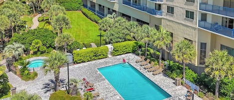 Un hotel con piscina rodeada de palmeras y sillas de descanso.