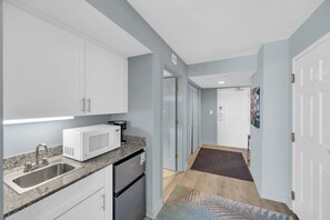 A modern kitchen with white cabinets, a stainless steel sink, a microwave, and a refrigerator.