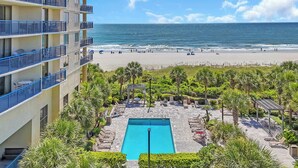 A hotel with a pool, beach view, and outdoor seating area.