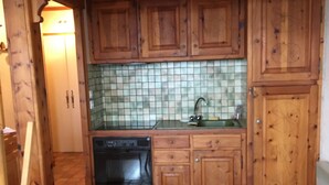 A compact kitchen with wooden cabinets, a tiled backsplash, and a built-in dishwasher. - 3-room apartment with balcony and parking in Samoëns (Samoëns)