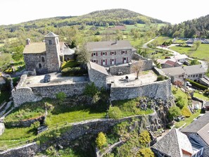 A stone castle with a central courtyard, surrounded by lush greenery and a hilly landscape. - Family cottage with yard, ping-pong, near Lyon and Clermont-Ferrand (Mézères)