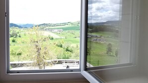 A room with a large window offering a view of a green landscape with fields, trees, and distant hills. - Family cottage with yard, ping-pong, near Lyon and Clermont-Ferrand (Mézères)