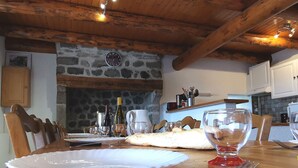 A wooden dining table with a white plate, fork, and glass, set in a rustic room with stone walls and wooden beams. - Family cottage with yard, ping-pong, near Lyon and Clermont-Ferrand (Mézères)