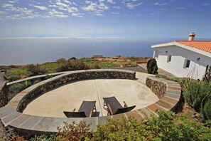 Un patio circular con dos sillones, un muro de piedra y vista al mar.