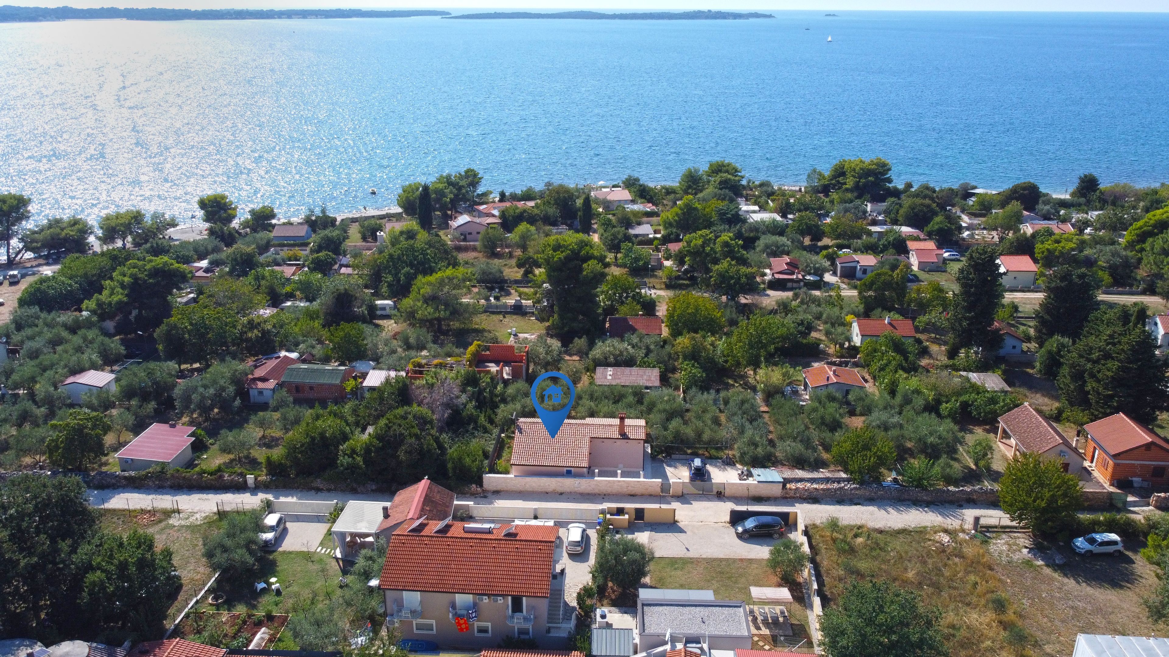 Una vista aerea di una zona residenziale costiera con case, alberi e una spiaggia che si apre sul mare.