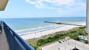 Ein Balkon mit Blick auf einen Strand, eine Mole, einen Parkplatz und einen Pool.