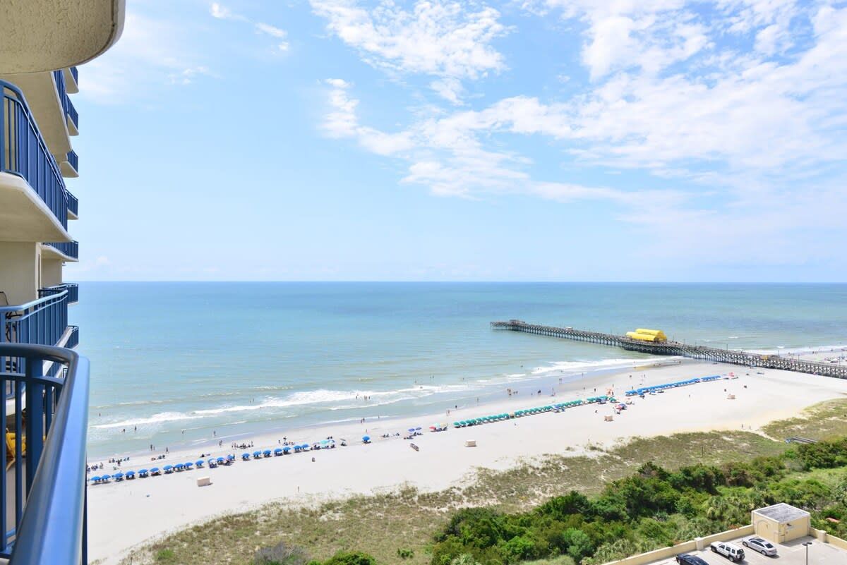 A beach with a pier extending into the water, a clear sky, and a view of the ocean.