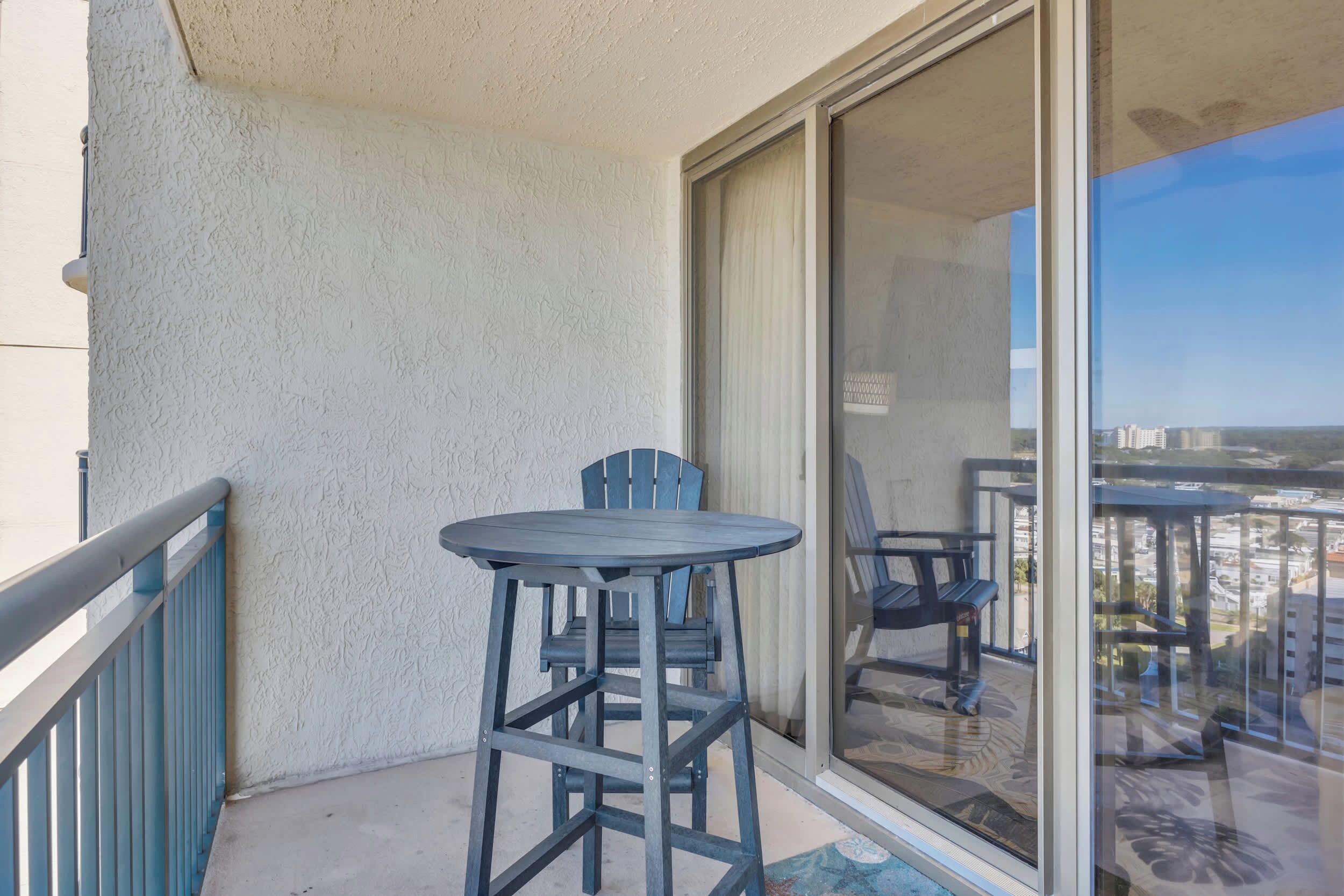 A balcony with a table and chairs, a sliding glass door, and a view of the cityscape.