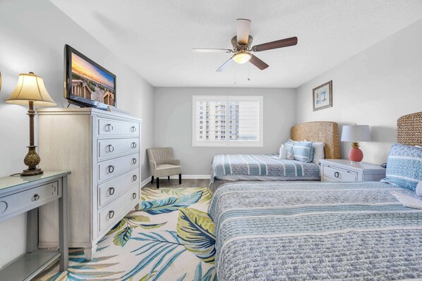 Une chambre à coucher comprenant un lit, un bureau, une chaise, un ventilateur de plafond, une fenêtre et une table de chevet.