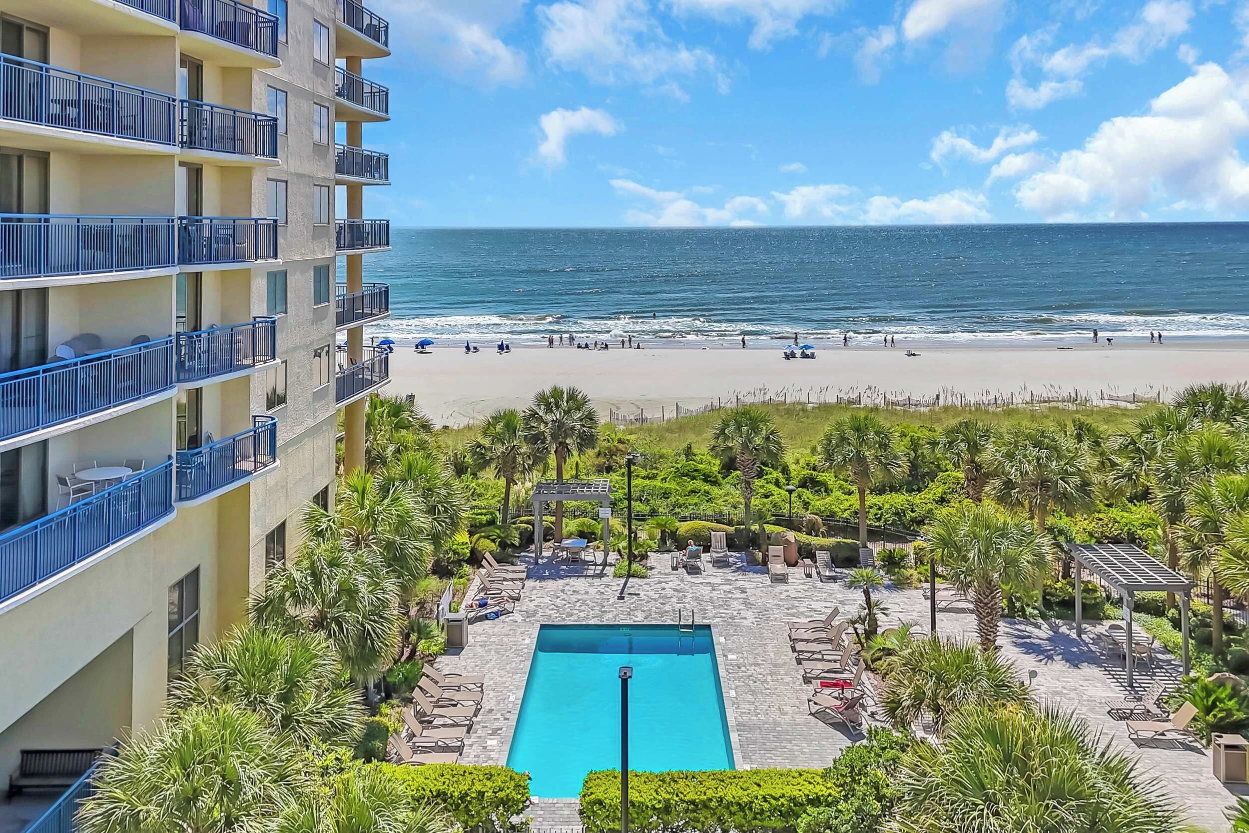 A hotel with a pool, beach view, and outdoor seating area.