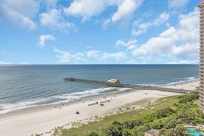 A beach with a pier, a pool, and a hotel building.