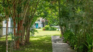 Un sendero bordeado de árboles y vegetación, que conduce a una casa con puerta azul y valla blanca.