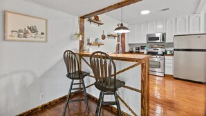 Una cocina con armarios blancos, una mesa de madera, dos sillas y una lámpara colgante.