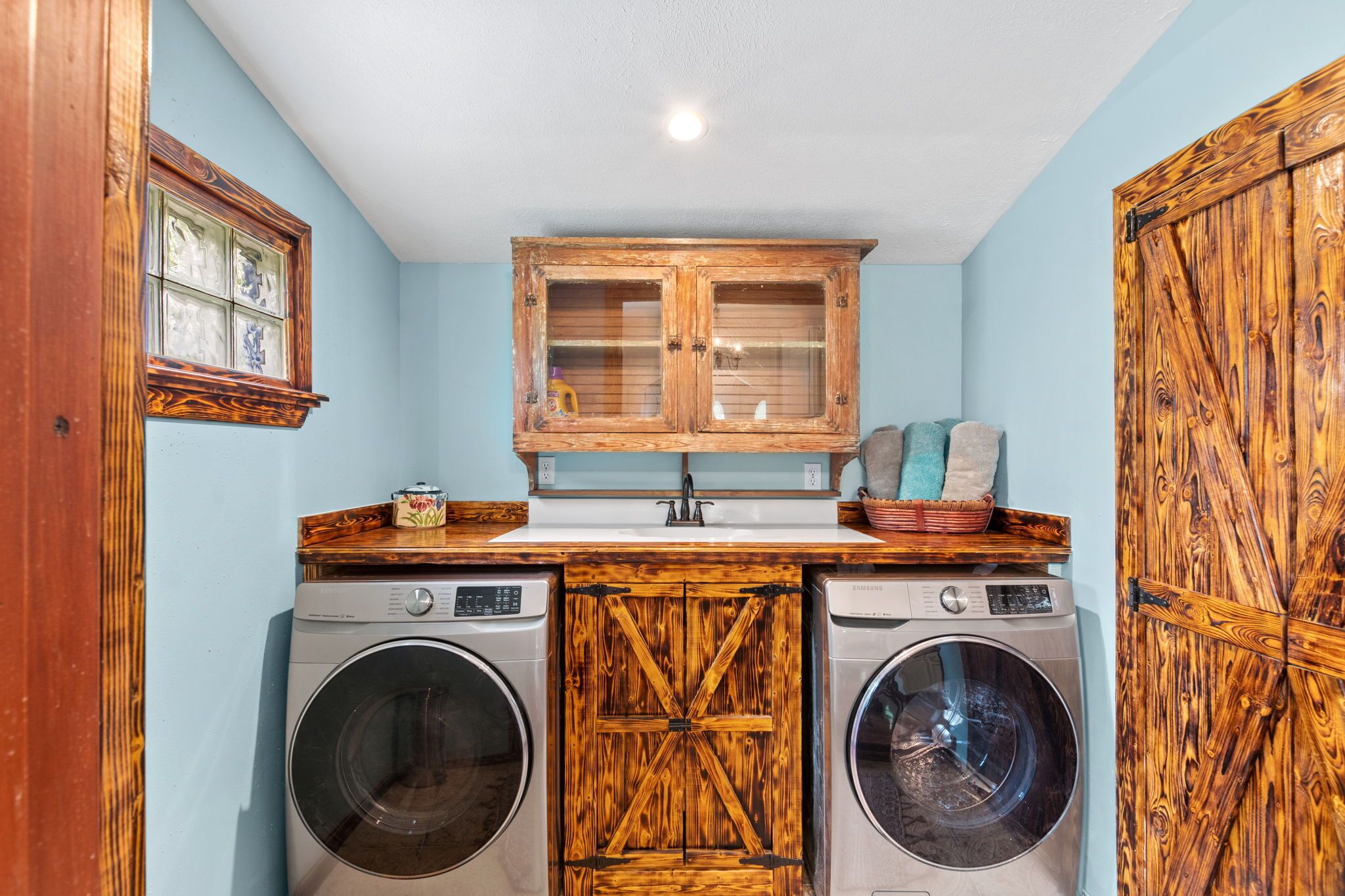 A laundry room with two front-loading washing machines, a wooden cabinet with glass doors, and a rustic wooden door.