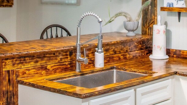 Una cocina con encimera de madera, un lavamanos de acero inoxidable, un grifo moderno y una lámpara colgante.