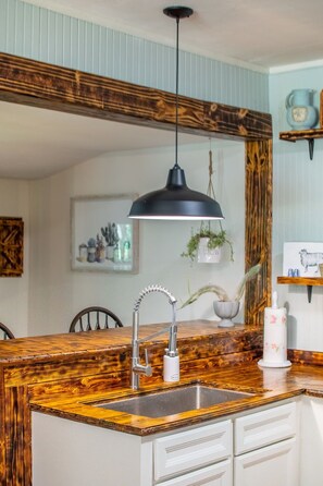 A kitchen with a wooden countertop, a stainless steel sink, a modern faucet, and a pendant light. - The Second-to-None Cracker Shack in Downtown Trenton (Trenton)
