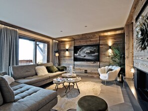 Ein modernes Wohnzimmer mit einer Couch, Sesseln, einem Couchtisch und einem an einer Holzwand montierten Fernseher.