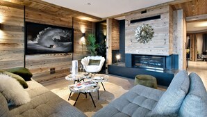 A modern living room with a fireplace, wooden walls, and a large TV. - Méribel: 140sqm Apartment, 4 Bedrooms, Ski Access, Fireplace, WIFI, Parking (Méribel)