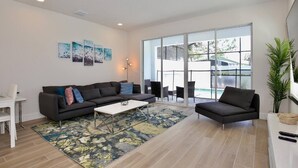 A spacious living room with a large window, a sofa set, a coffee table, and a small table with a chair. - Great NEW 4 bedroom townhouse in Hidden Forest, with private pool! (Clermont)