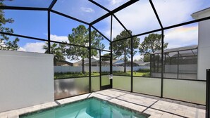 A swimming pool with a glass enclosure, surrounded by a patio area with a view of trees and a clear sky. - Great NEW 4 bedroom townhouse in Hidden Forest, with private pool! (Clermont)