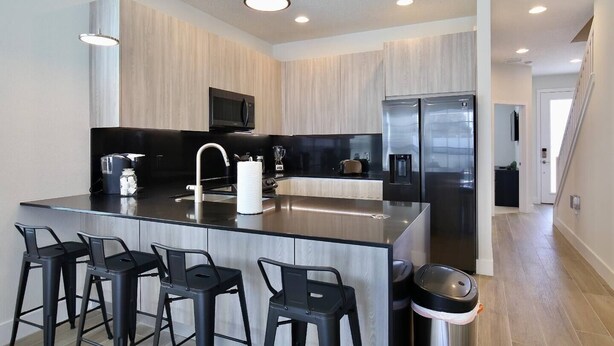 A modern kitchen with a central island, black bar stools, stainless steel appliances, and a microwave above the island. - Great NEW 4 bedroom townhouse in Hidden Forest, with private pool! (Clermont)
