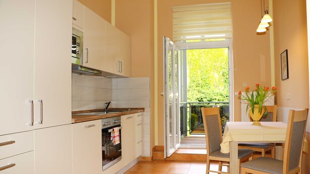 Een keuken met witte kastjes, een fornuis en een eethoek met een tafel en stoelen.