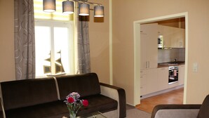 Een moderne woonkamer met een bank, een glazen salontafel en uitzicht op een keuken door een open doorgang.