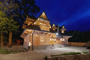 A log cabin with a stone foundation, multiple gabled roofs, and a well-lit exterior. - House for 14 People in Zakopane | 2 Saunas | Fireplace (Zakopane)