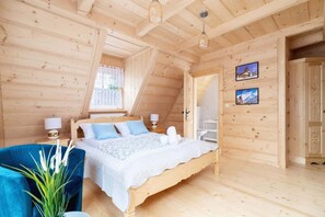 A wooden cabin bedroom with a bed, bedside tables, a chair, and a window. - House for 14 People in Zakopane | 2 Saunas | Fireplace (Zakopane)
