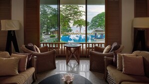 Une pièce meublée de mobilier en osier, avec une petite table ronde et une vue sur une piscine et des arbres.