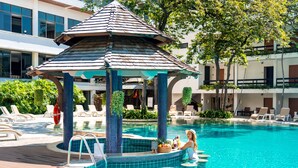 Un espace piscine agrémenté d’un kiosque, de chaises longues et d’une végétation luxuriante évoquant les tropiques.