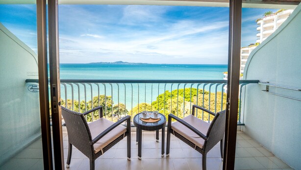 Un balcon agrémenté de meubles en osier, une petite table et une vue sur la mer et le paysage lointain.