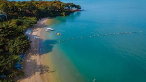 Une vue aérienne d’une plage où un bateau est amarré près du rivage, entouré d’une végétation luxuriante et d’une eau d’un bleu limpide.