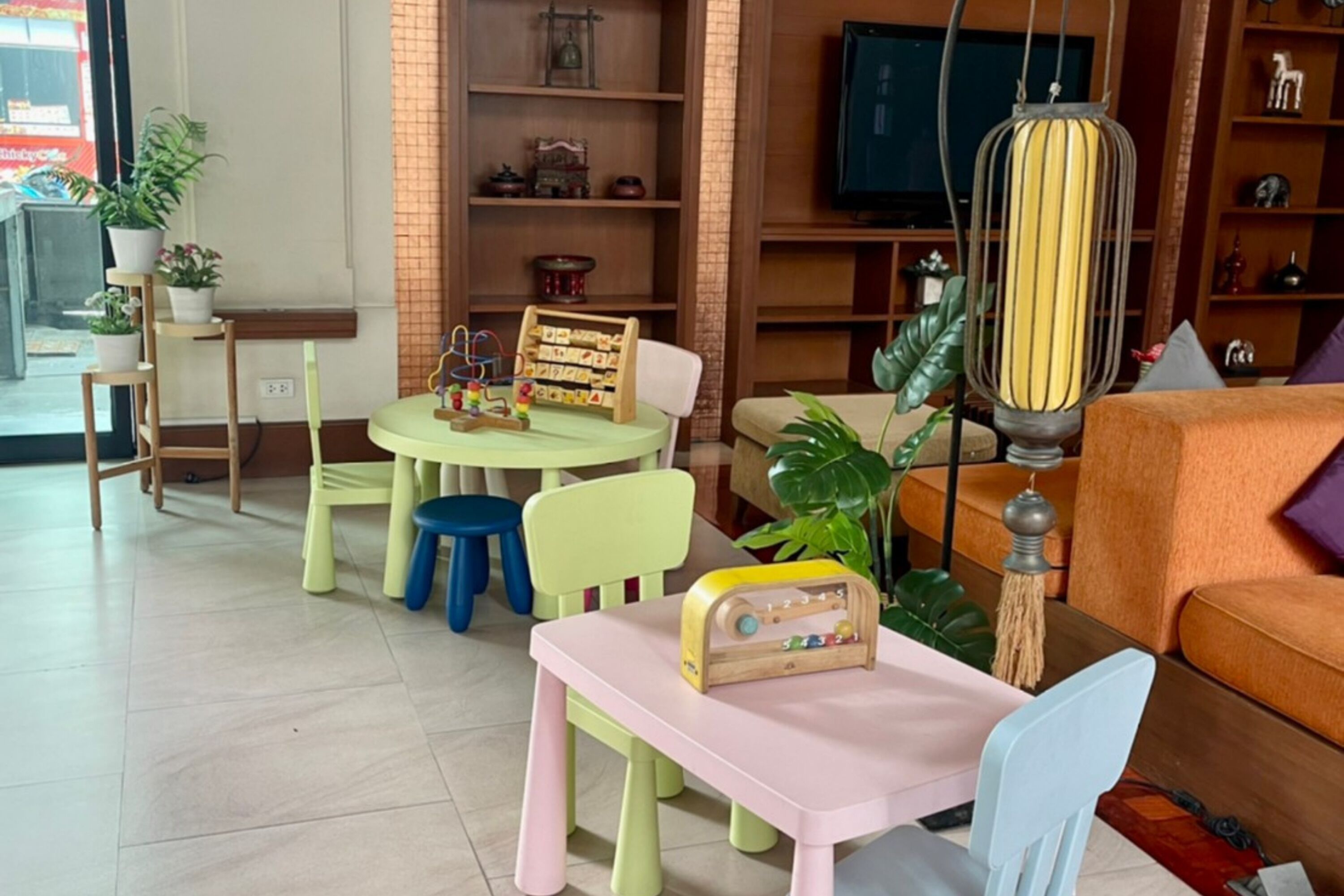 A cozy living room with a pink table, a blue chair, a wooden radio, and a television on a wooden stand.