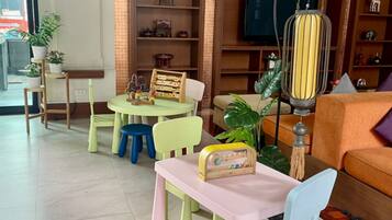 A cozy living room with a pink table, a blue chair, a wooden radio, and a television on a wooden stand.
