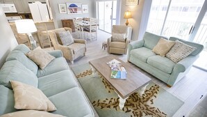 Un vaste espace de vie comprenant un ensemble de canapés, une table basse et une table à manger avec des chaises. De grandes fenêtres offrent une vue sur l’extérieur.