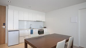 Una cocina moderna con armarios blancos, horno empotrado y un comedor con mesa y sillas de madera.